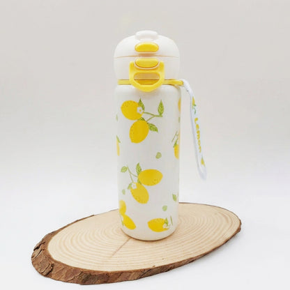 A white insulated water bottle with a yellow lemon print, featuring a flip-top lid with yellow accents and a matching carrying strap, displayed on a round wood slice against a light gray background.