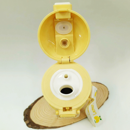 A yellow reusable water bottle lid shown open, photographed on a light neutral background with a wood slice prop and a small printed tag attached.